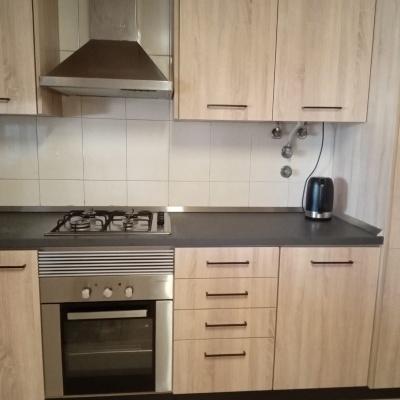 Cozinha com móveis em madeira clara, forno e placa a gás inox, exaustor e chaleira preta na bancada