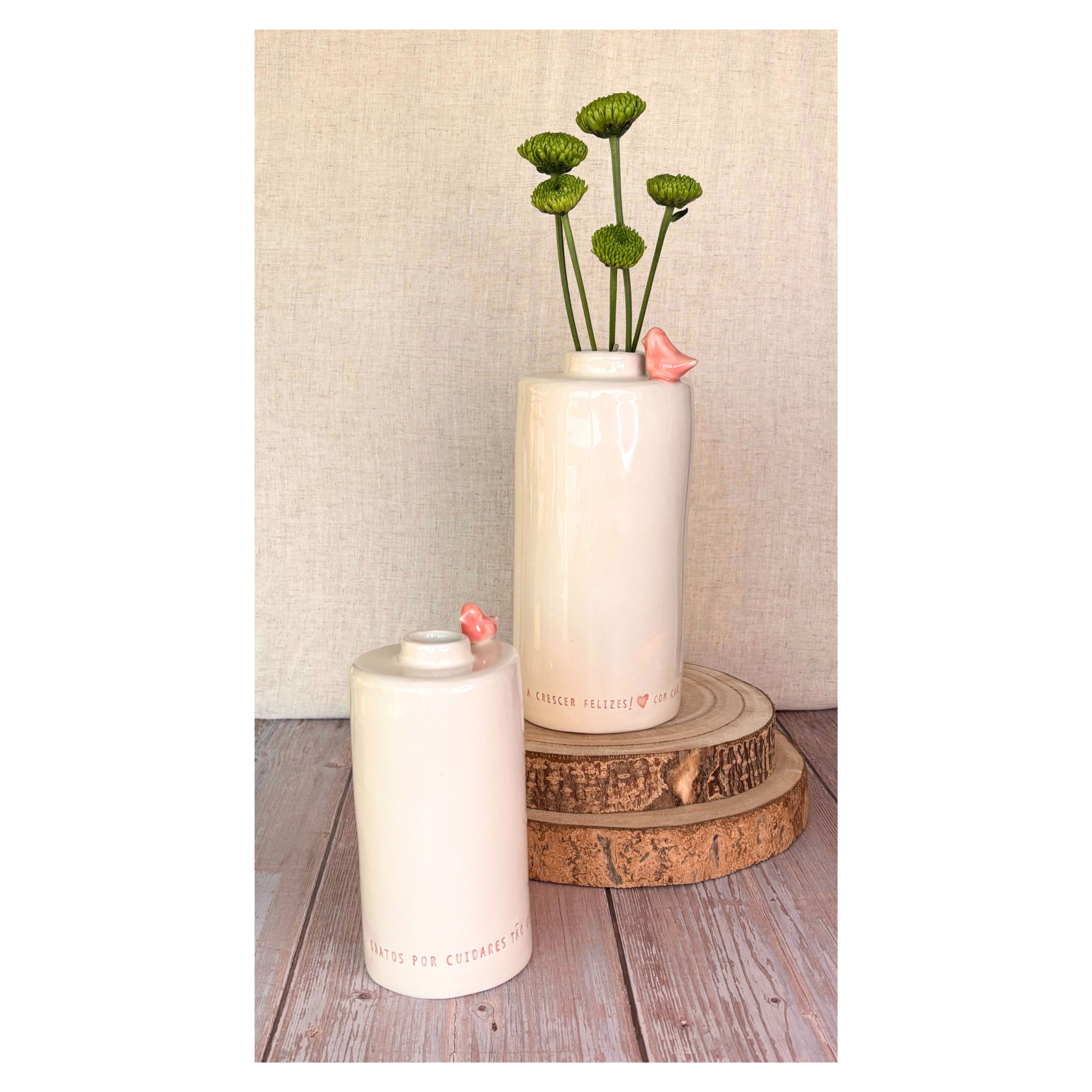 Jarra Grande Personalizada Dois vasos cerâmicos brancos com flores verdes e detalhes rosa, sobre tábuas de madeira, fundo bege.