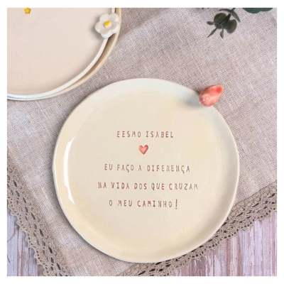 Pratos de cerâmica creme com detalhes florais e texto sobre tecido bege e madeira