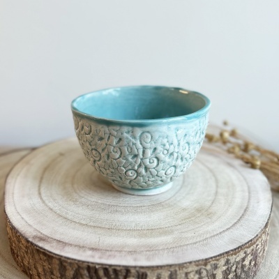 Taça azul clara em cerâmica com padrão em relevo sobre base de madeira