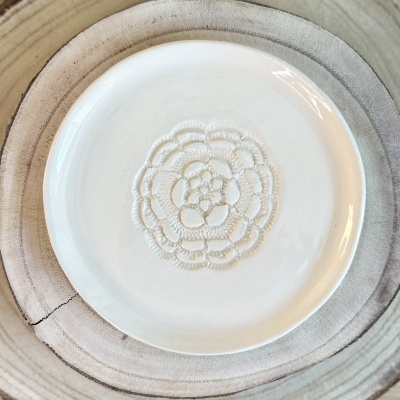 Prato branco de cerâmica com relevo em flor sobre superfície de madeira