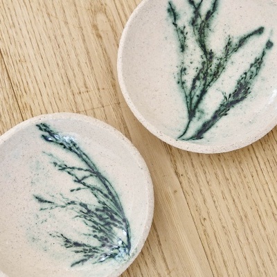 Dois pratos pequenos de cerâmica branca com padrão verde em forma de ramo sobre madeira clara.
