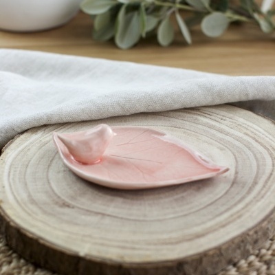 Pequeno prato rosa em forma de folha com pássaro numa base de madeira redonda