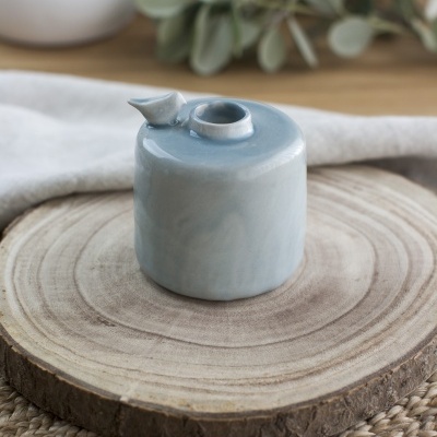Pequeno recipiente cerâmico azul claro com bico, sobre tábua de madeira redonda