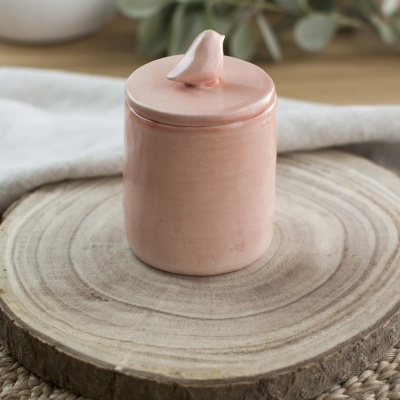 Frasco pequeno de cerâmica rosa com tampa em forma de gota sobre base de madeira