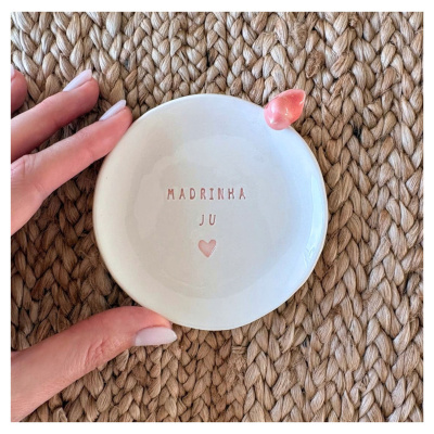 Prato branco cerâmico com texto e decoração rosa sobre superfície trançada castanha.