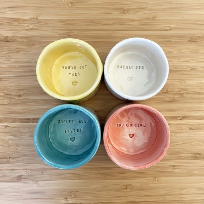 Conjunto de quatro recipientes de cerâmica coloridos com textos motivacionais no interior