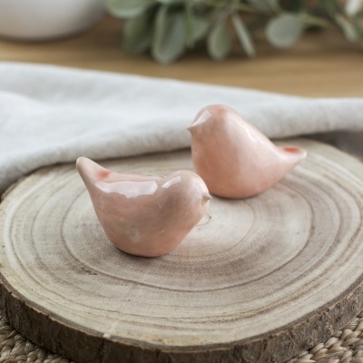 Duas figuras de pássaros cor de rosa em cerâmica sobre base de madeira redonda