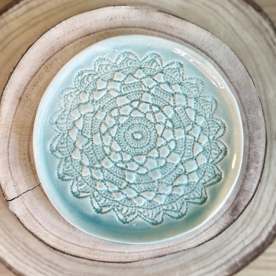 Prato cerâmico azul com padrão rendado colocado sobre base de madeira