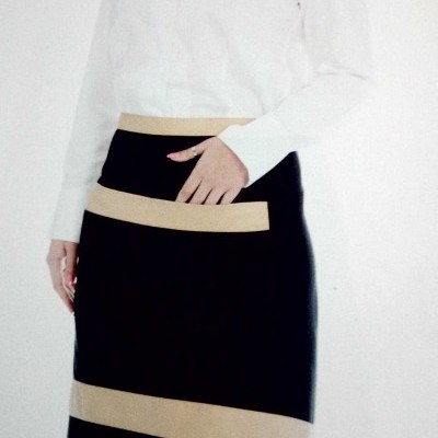 Mulher com camisa branca e saia preta com faixas bege