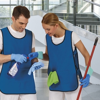Duas pessoas com coletes azuis, luvas e produtos de limpeza em edifício interior com escadas.