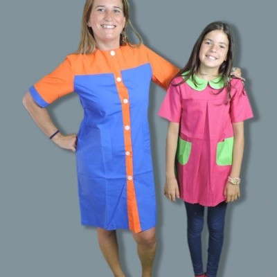 Mulher com vestido azul e laranja e criança com vestido rosa e verde em fundo cinzento