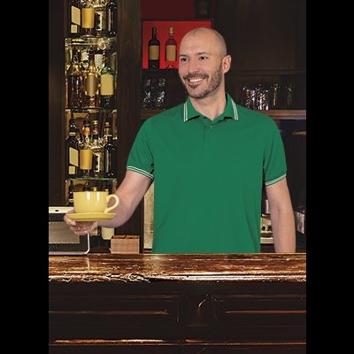 Homem de polo verde segurando chávena amarela num bar