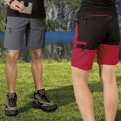 Dois homens com calções curtos e botas de caminhada numa paisagem com lago e montanhas