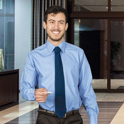 Homem com camisa azul clara e gravata azul escura junto a um cartão branco em ambiente interior elegante