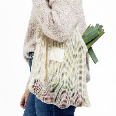 Saco de rede de algodão creme com legumes, usado por pessoa com camisola bege e jeans azul