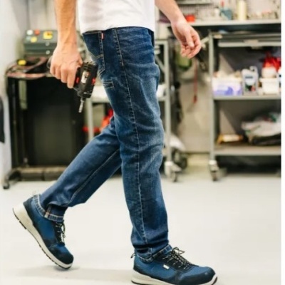 Pessoa calçando sapatos desportivos azuis e calças de ganga num ambiente de oficina