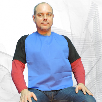 Homem sentado com babete azul sobre t-shirt preta e vermelha, calças jeans, fundo branco com padrões cinzentos