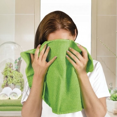 Mulher a cobrir o rosto com uma toalha verde numa casa de banho com decoração de toalhas e plantas