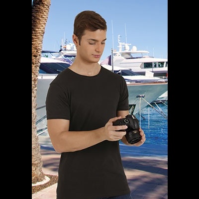 Homem com t-shirt preta segurando câmara fotográfica ao ar livre junto ao mar.