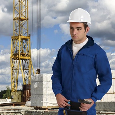 Homem com fato azul e capacete branco numa obra com grua e materiais de construção