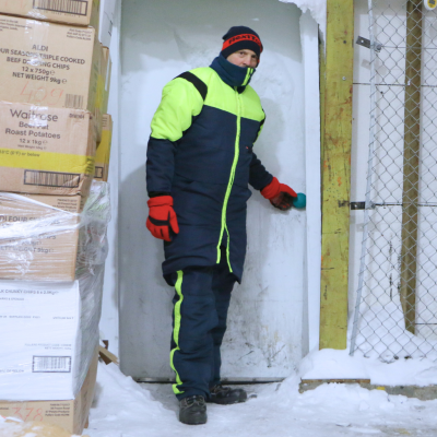 Homem em fato de trabalho a abrir porta branca numa área com neve e caixas empilhadas