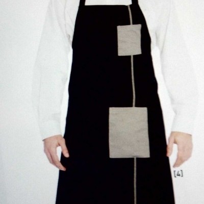 Homem com avental preto com bolsas cinzentas sobre camisa branca