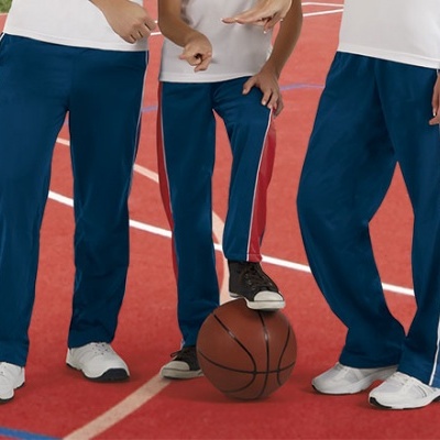 Três pessoas com calças desportivas azuis com riscas laterais, pé numa bola de basquetebol numa pista desportiva