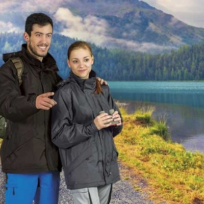 Casal com casacos impermeáveis pretos junto a lago e montanhas