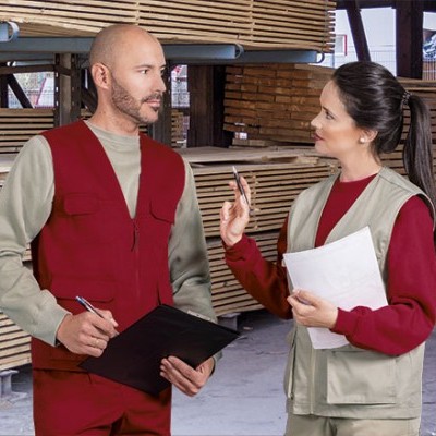 Trabalhadores com coletes vermelhos e beges num armazém de madeira