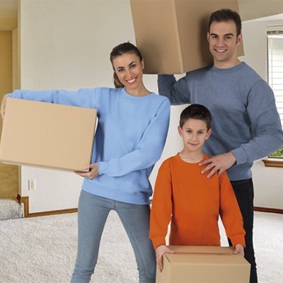 Família em casa segurando caixas de cartão, com camisolas azul claro, cinza e laranja.