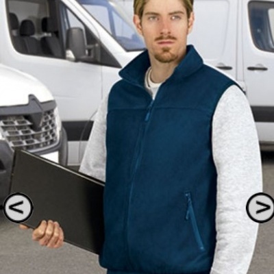 Homem com colete azul e camisola cinza segurando pasta preta perto de carrinhas brancas