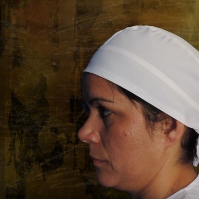 Pessoa com lenço branco amarrado na cabeça sobre fundo castanho