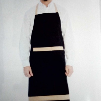 Homem vestido com avental preto com faixas bege e camisa branca