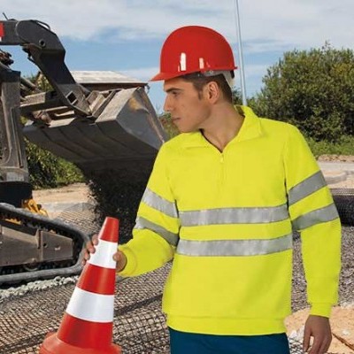Trabalhador com colete amarelo e capacete vermelho segurando cone de sinalização num estaleiro