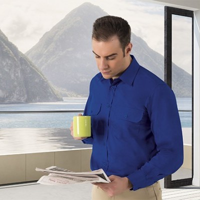 Homem com camisa azul e caneca amarela lendo jornal numa sala com vista para montanhas e lago.