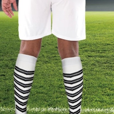 Jogador de futebol com calções brancos, meias riscas pretas e chuteiras laranja a segurar bola preto e branca.