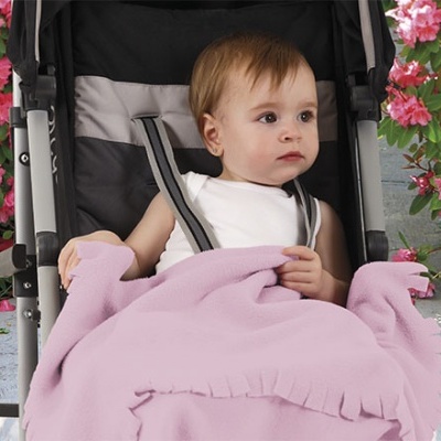 Bebé num carrinho preto e cinza coberto com manta rosa rodeado de flores.