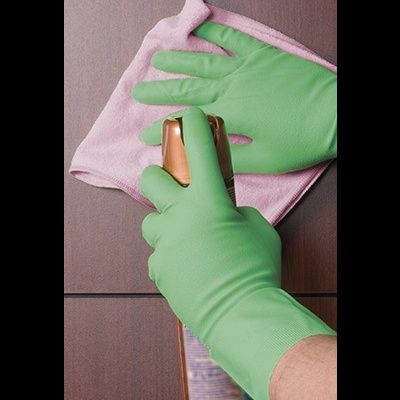 Mãos com luvas verdes segurando spray dourado e pano rosa sobre madeira
