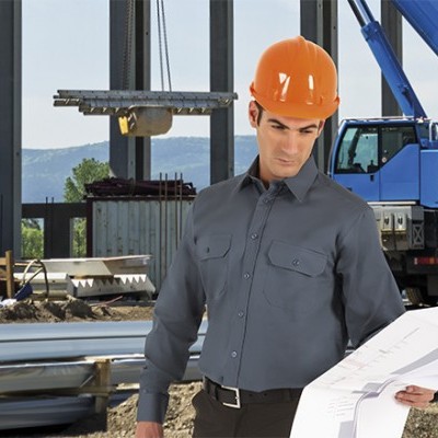 Homem com camisa cinza e capacete laranja em obra com guindaste