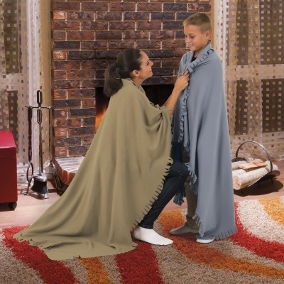 Mulher e criança com mantas bege e azul clara junto à lareira num ambiente acolhedor com tapete colorido e tijolos.