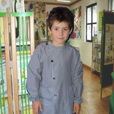 Menino com camisola xadrez azul e branco em ambiente escolar com chão de madeira.