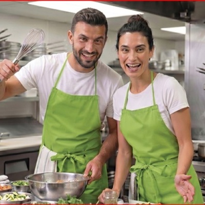 Dois chefs com aventais verdes numa cozinha profissional preparando alimentos