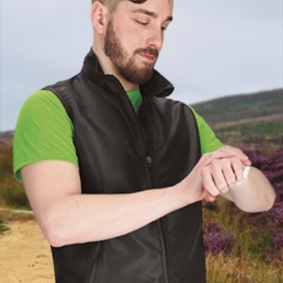 Homem com colete preto e t-shirt verde numa paisagem exterior