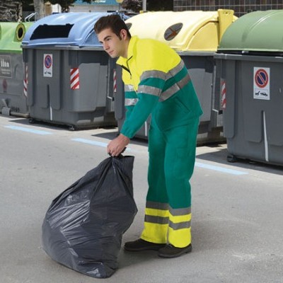 Homem com roupa de trabalho a segurar saco de lixo perto de contentores de reciclagem