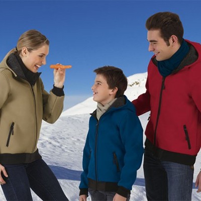 Três pessoas com casacos polares coloridos ao ar livre na neve, com boneco de neve ao fundo.