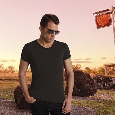 Homem com t-shirt preta e óculos de sol junto a bomba de gasolina antiga ao pôr do sol