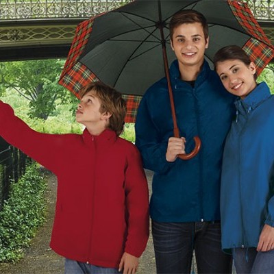 Três pessoas com casacos impermeáveis coloridos e um guarda-chuva xadrez em ambiente ao ar livre.