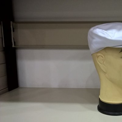 Boné tipo boina branco em manequim amarelo numa prateleira.