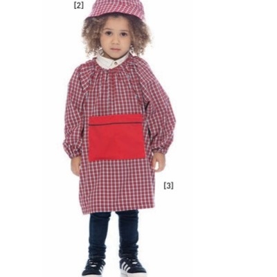 Criança com fato escolar xadrez vermelho e branco com avental e chapéu combinando, calças pretas e ténis no fundo branco